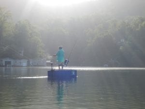 A fisherman casting his line on a blue round boat in bright sunlight.