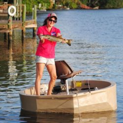 A female fisherman with a snook caught by a dock on a tan round boat