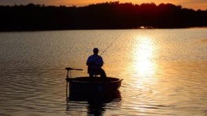A man fishing in a one man boat at sunset