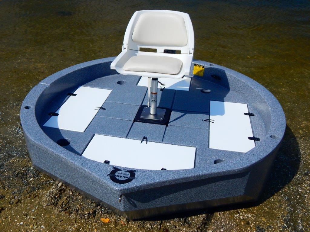 This is a top view of a slate colored round boat with white trim sitting on the shore