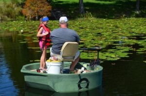 A father and daughter fishing from a green round boat for bass while both on the boat at the same time