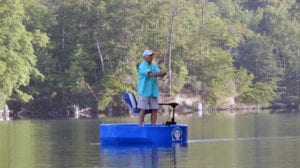 fisherman casting his rod towards the shore while standing on the deck of a blue round boat