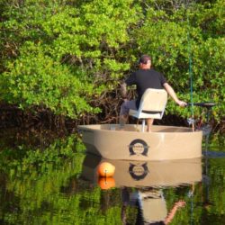 Fisherman driving a round boat near the shoreline with an electric trolling motor.